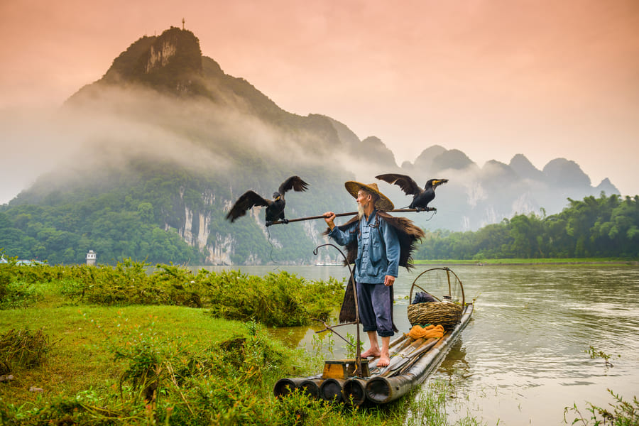 Paisaje de río yangshuo con montaña y un atardecer cálido con una persona nativa navegando tranquilamente